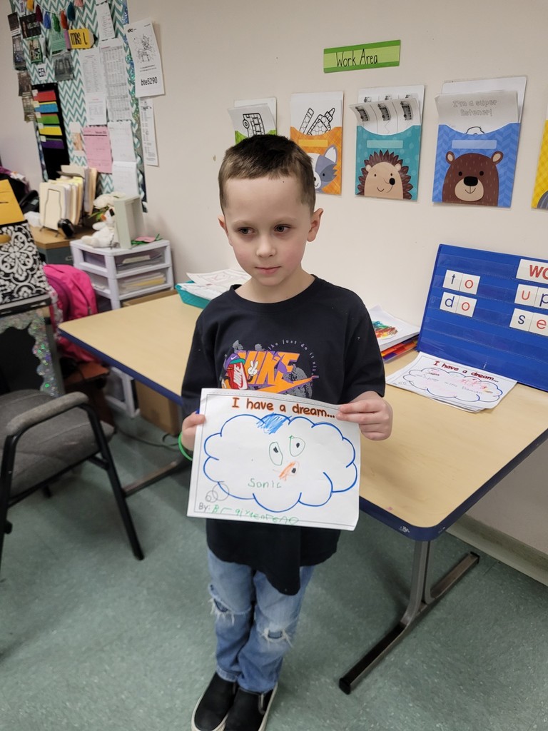 Young boy in a black graphic shirt is holding his paper up hat he colored.