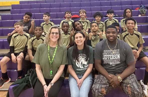 Group of kids and adults wearing green and smiling while they sit on the bleachers. 