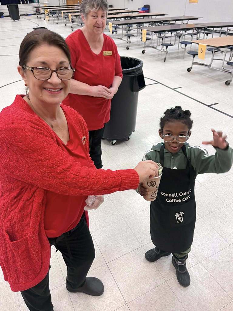 A women in red putting money into a cup a young boy is holding. 