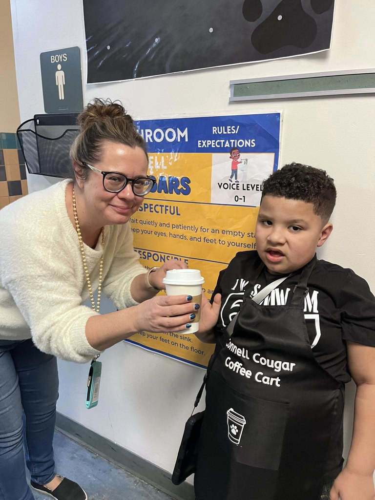 A student handing an adult a cup of coffee. 