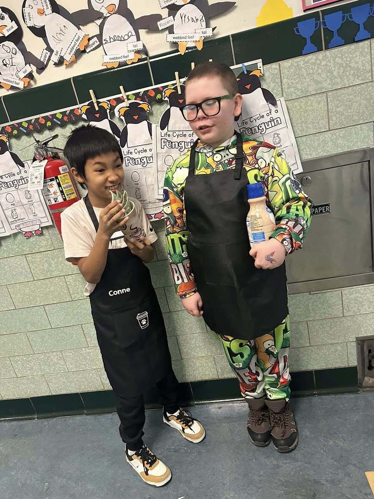 Kids wearing aprons while they hold creamer and money in a cup.