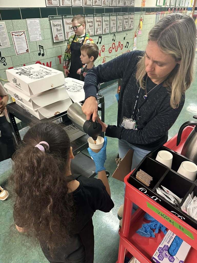 An adult pouring coffee into a cup that a young girl is holding. 