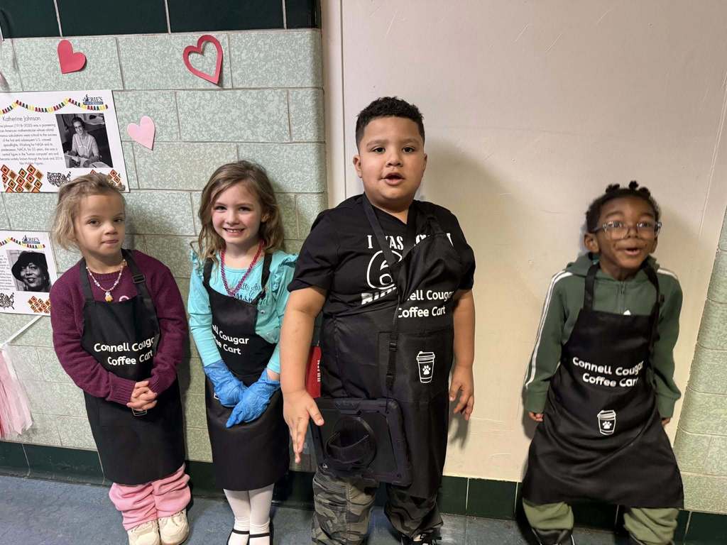 Kids wearing aprons and smiling in the hall. 