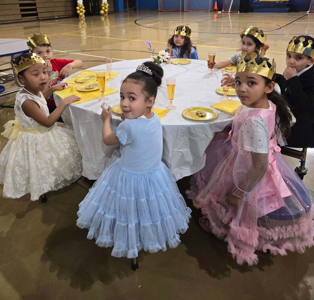 Young girls in princess dresses and crowns eating at a table.