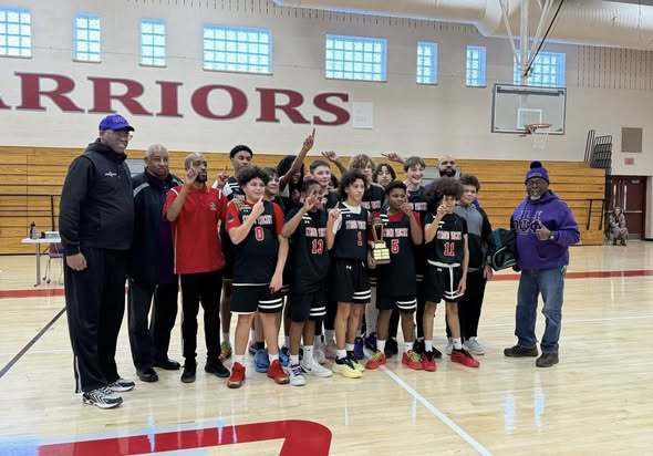 A group of boys on a team and adults standing next to them on a basketball court. 