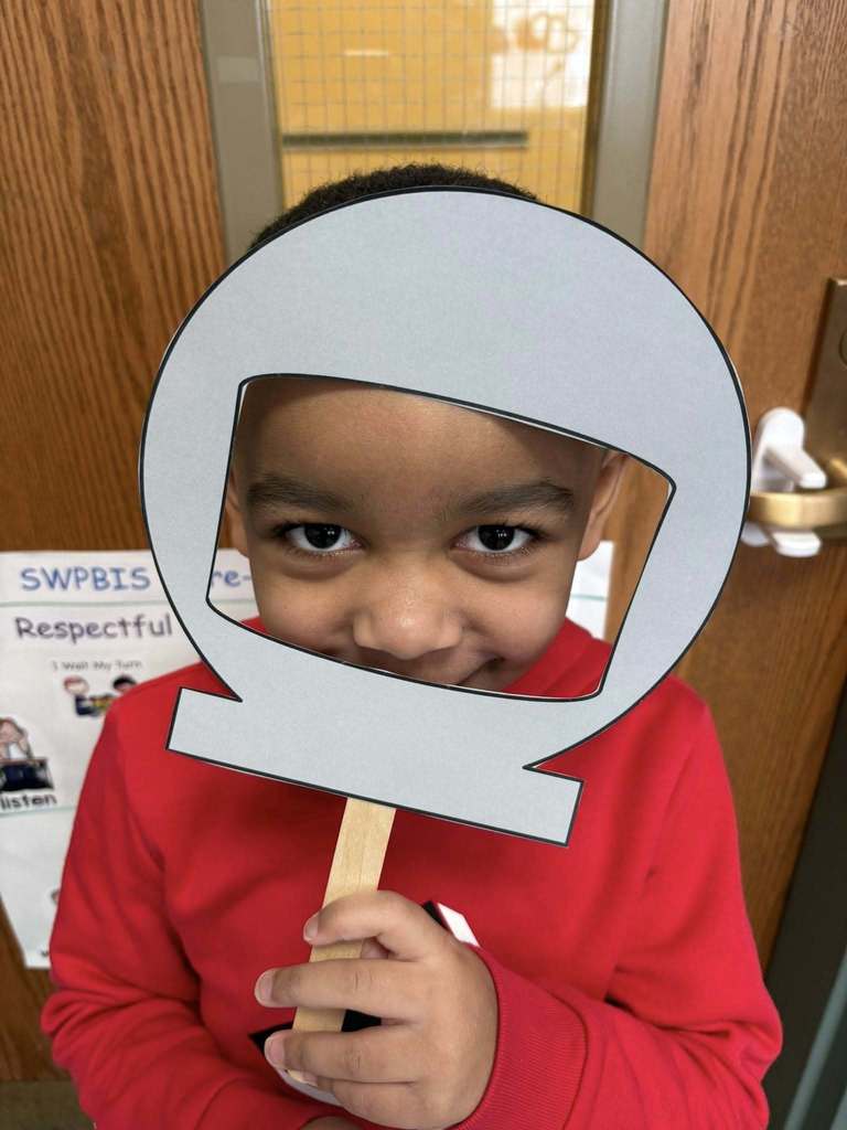Kid in a red shirt is holding up a cutout of a astronaut helmet on its face.
