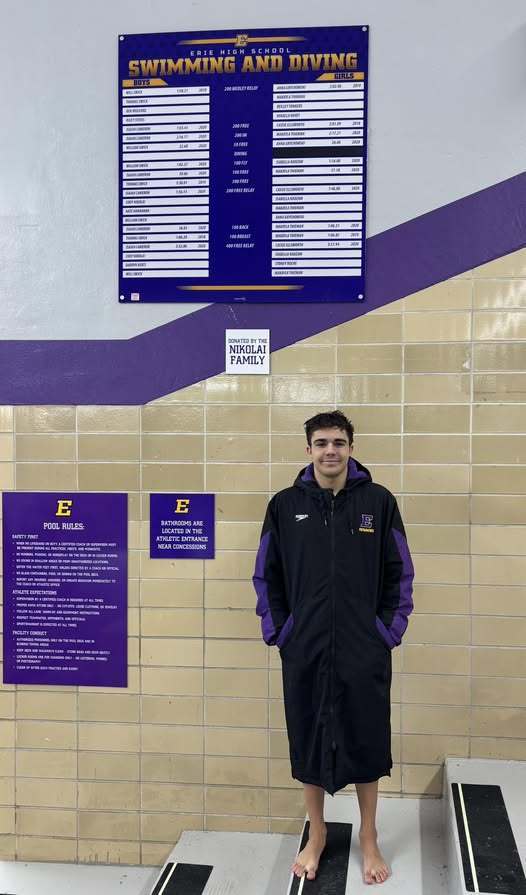 Young man standing and wearing a Erie High black and purple jacket.