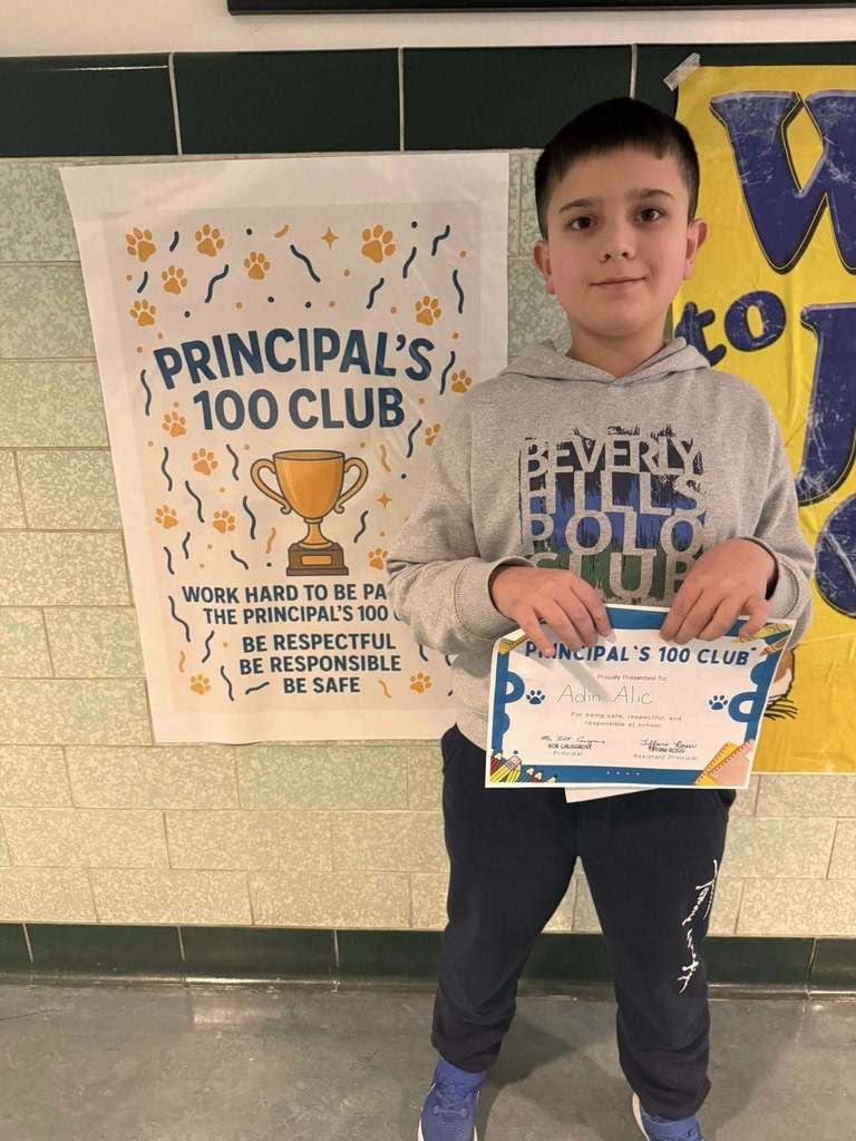 Young child dressed in a gray graphic hoodie is holding up their certificate. 