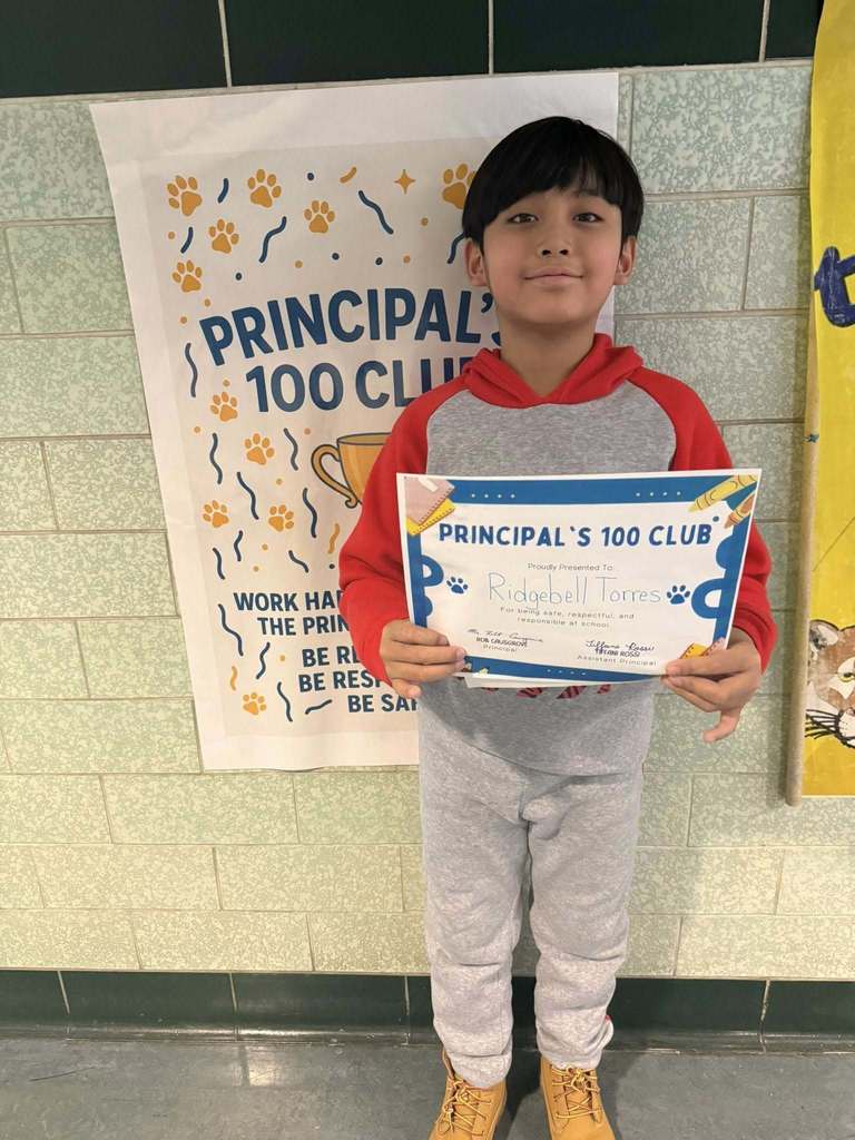 Young child dressed in a red and gray hoodie is holding up their certificate. 