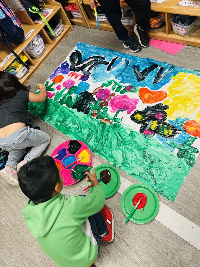 Kids are painting a Spring mural on a large piece of paper on the floor.