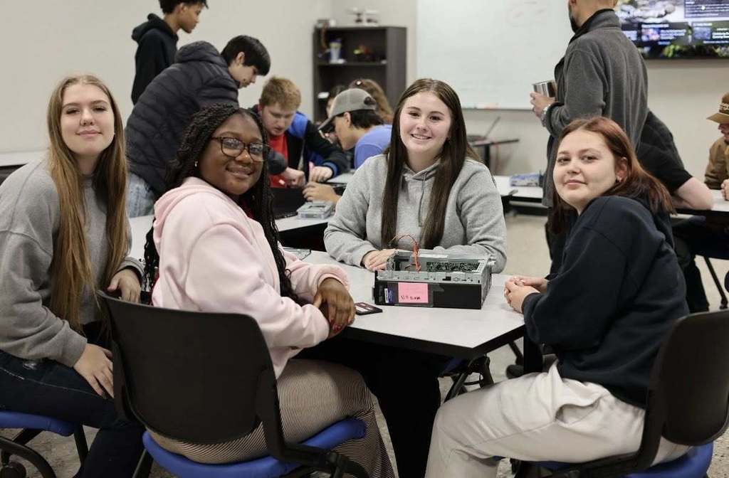 A group of students engaged in a classroom activity, seated around a table with a small box.