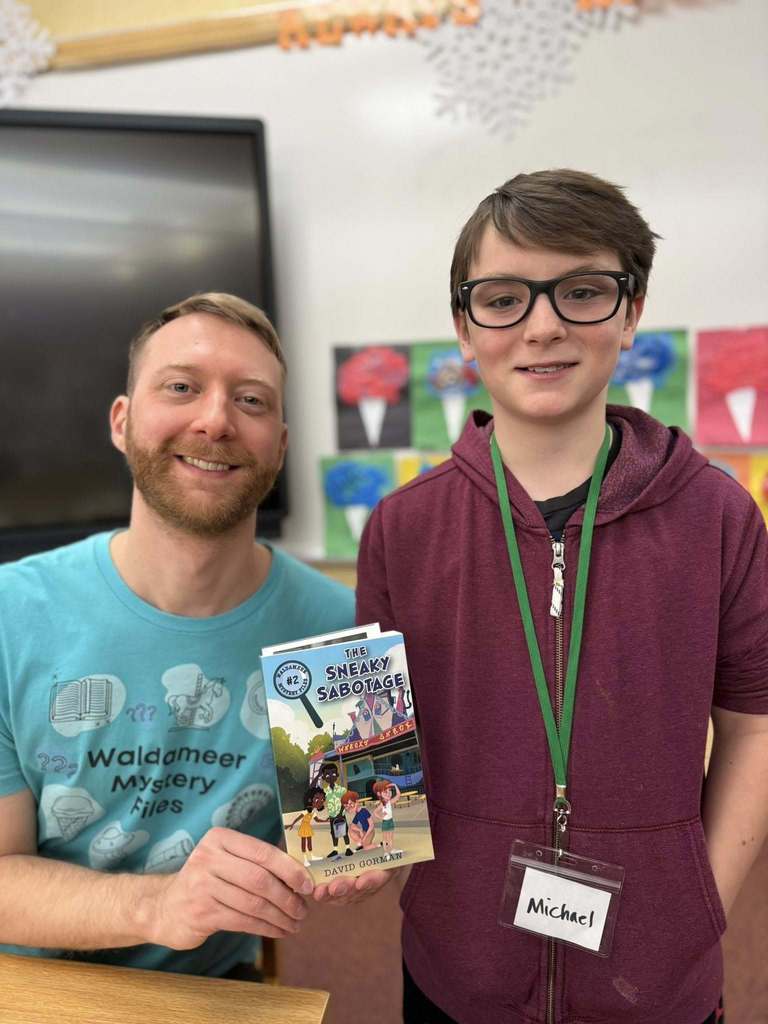 A man in a blue shirt is holding a book and smiling next to a kid in a red hoodie.