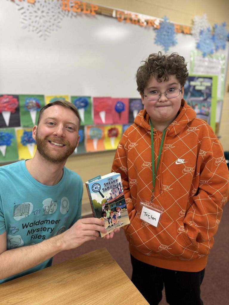 A man in a blue shirt is holding a book and smiling next to a kid in a orange hoodie.