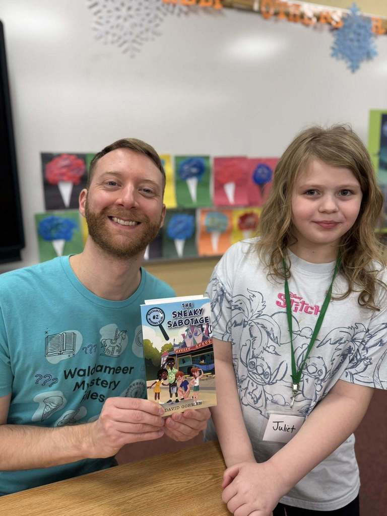 A man in a blue shirt is holding a book and smiling next to a kid in a gray graphic shirt.