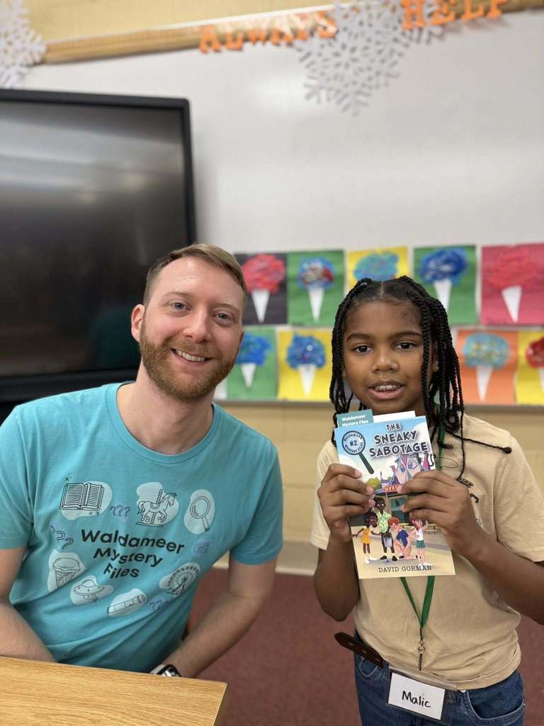 A man in a blue shirt is next to a kid that is holding a book.