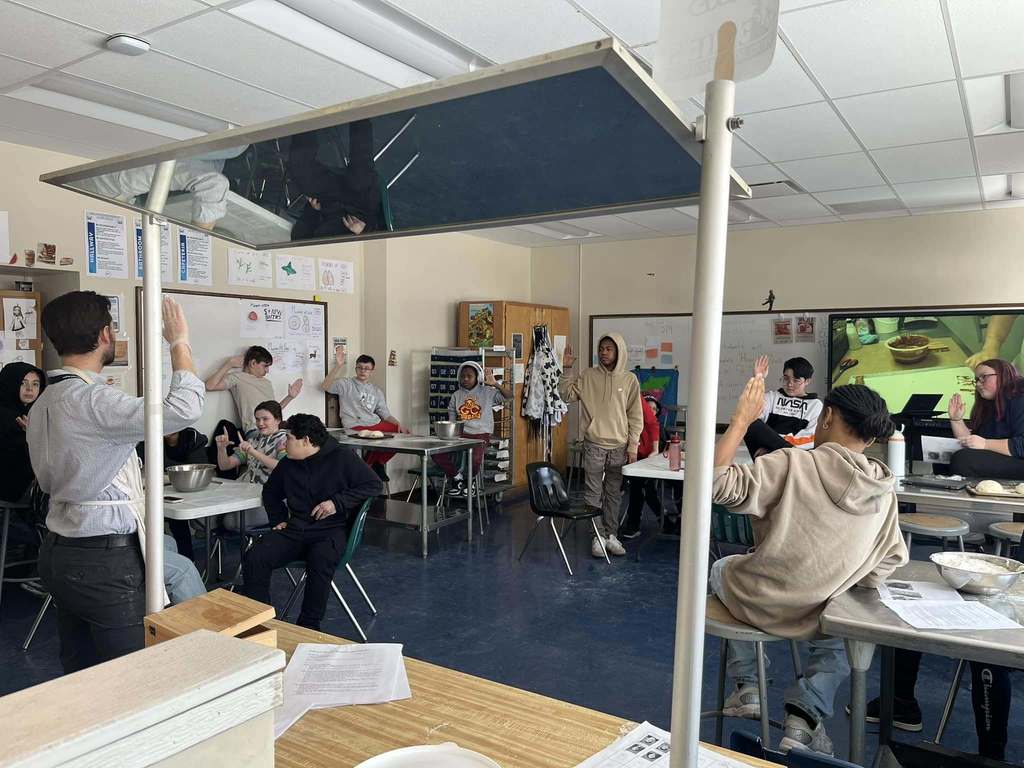 Kids in a classroom and they have their hands raised. 
