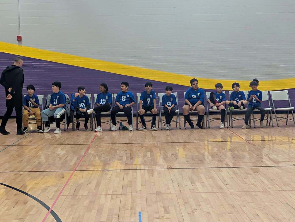 Kids sitting on chairs while they wear their team jerseys.