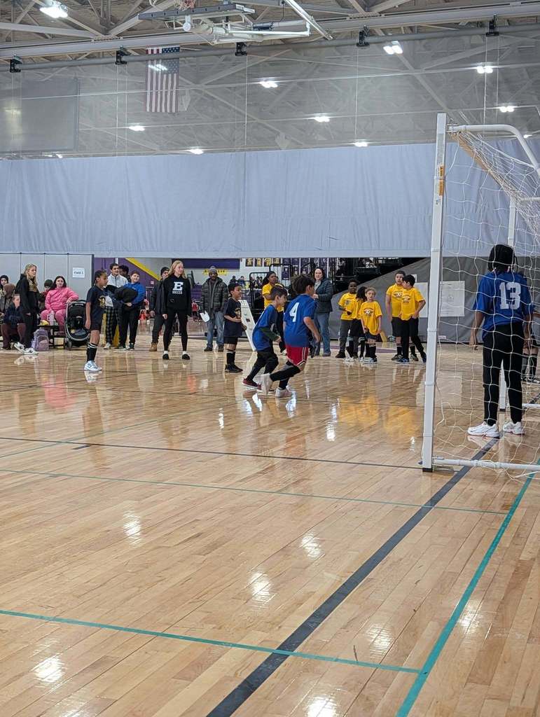 Kids playing soccer in a school gym.