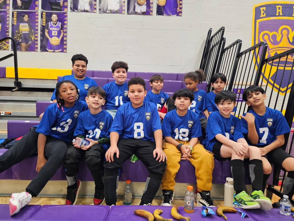 Group photo of students in matching blue jerseys sitting on purple bleachers.