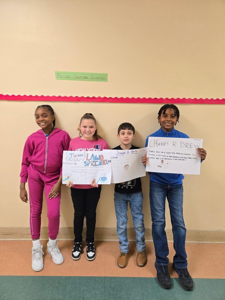 A group of students holding up white paper that has drawings and writing on it.