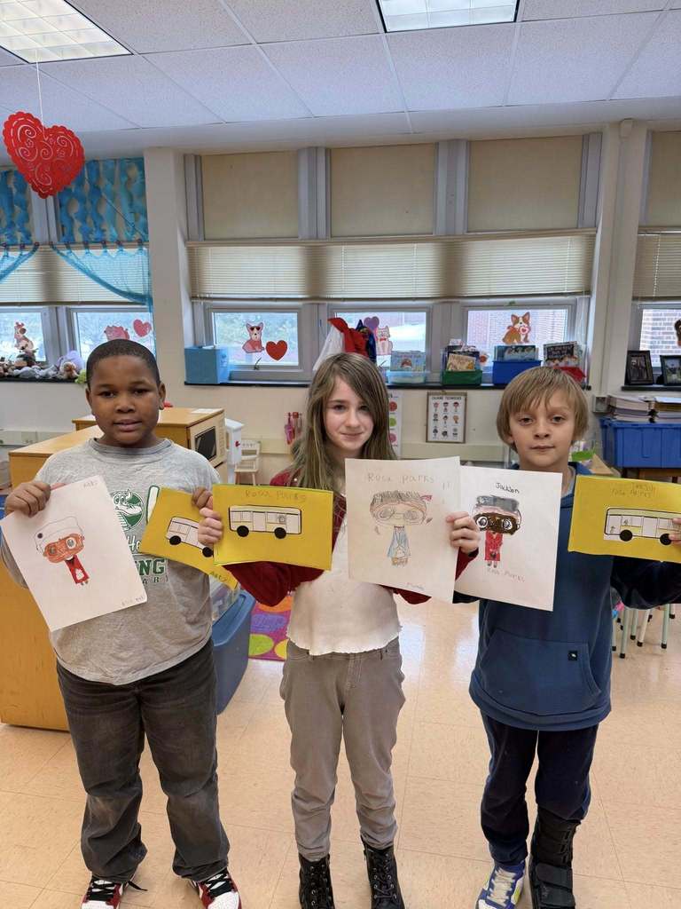 A group of students holding up white paper that has drawings and writing on it.