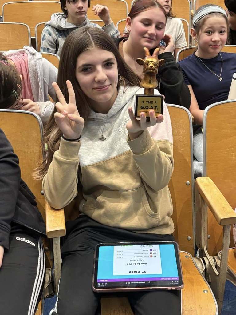 Young girl holding a trophy in one hand while holding two fingers up with her other hand. 