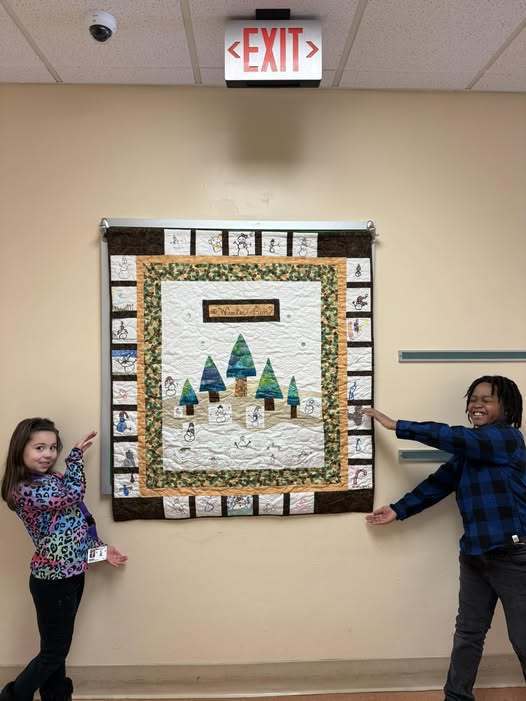 Two students pointing to a piece of art on the wall that has trees in the snow on it.