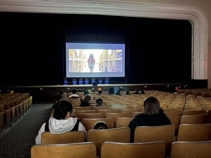 People sitting in an auditorium and watching a movie on a large screen.