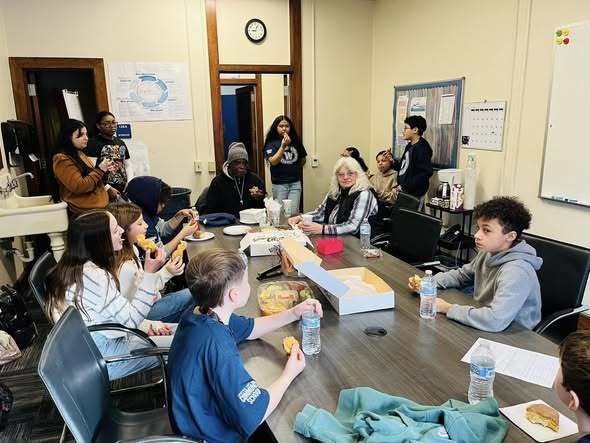 Group of students and adults eating donuts at a large table.