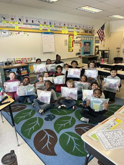 Students in a classroom holding up bags with stuff in them. 