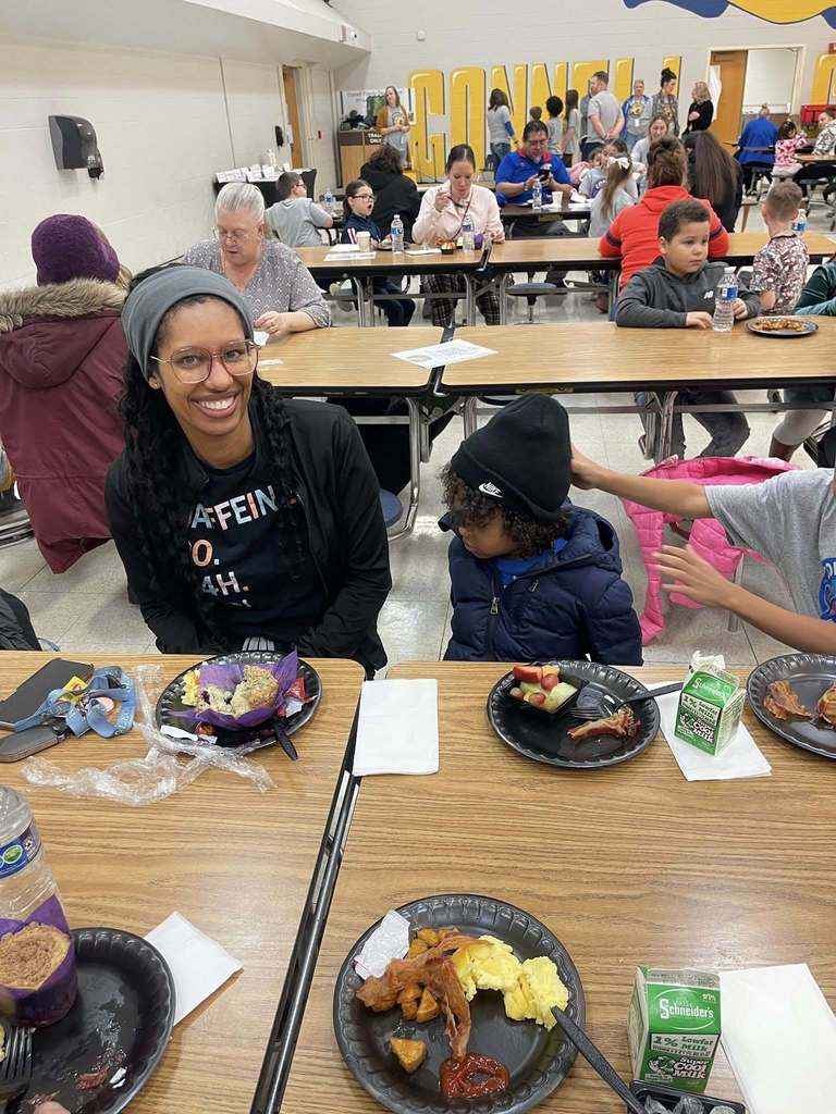 A women and kids sitting at a table in a school cafeteria.
