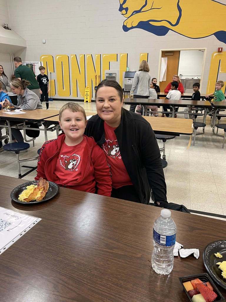 A women and young boy in matching red shirts smiling in a school cafeteria. 
