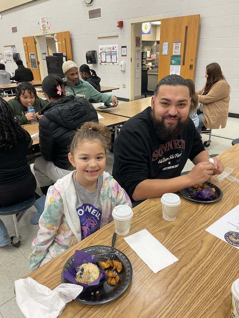 A man and young girl are smiling in a school cafeteria. 