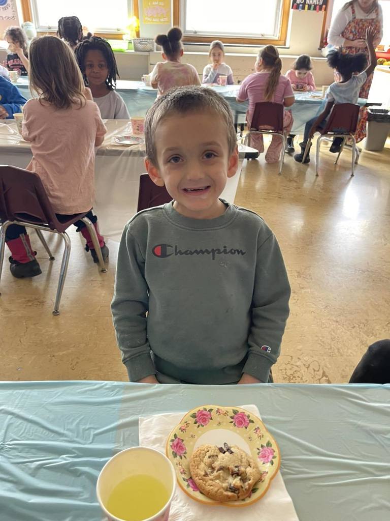 Young boy smiling with a cookie and a cup of juice in front of him. 