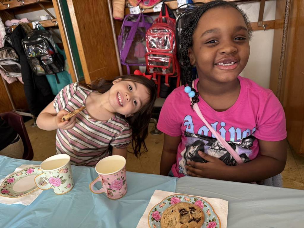 Two girls smiling and holding qith one of the girls holding her cookie. 