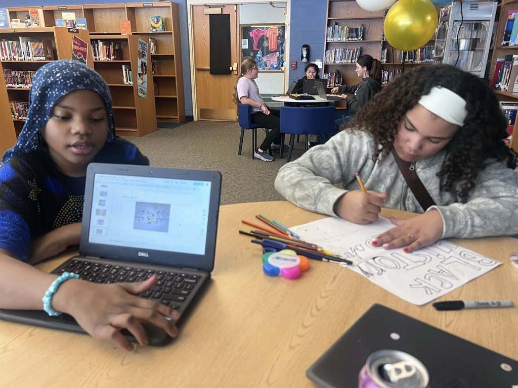 Kids working on laptops and drawing on paper in a library. 