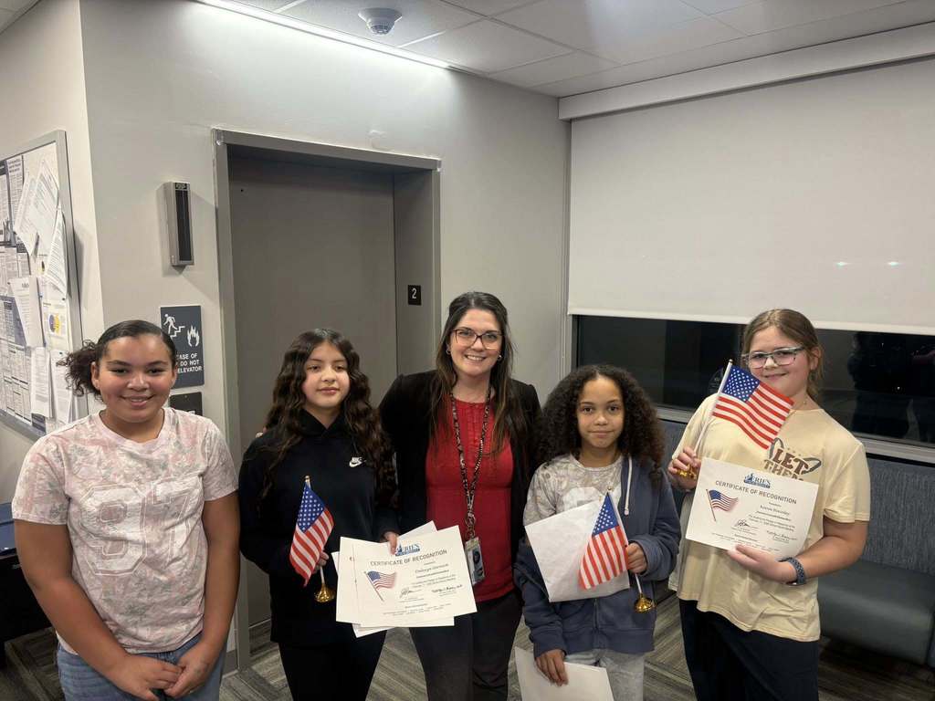 Kids smiling next to an adult while they hold their certificates and flags. 