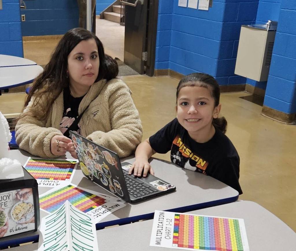Young child smiling and working on a laptop while they sit next to an adult.