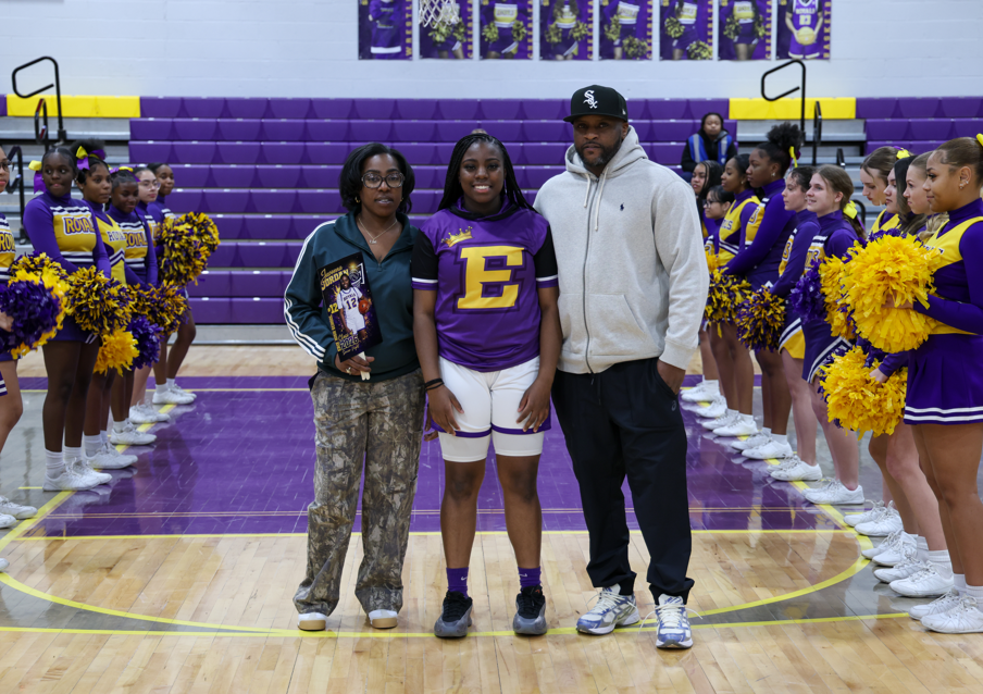 A student in her team uniform standing with her parents.