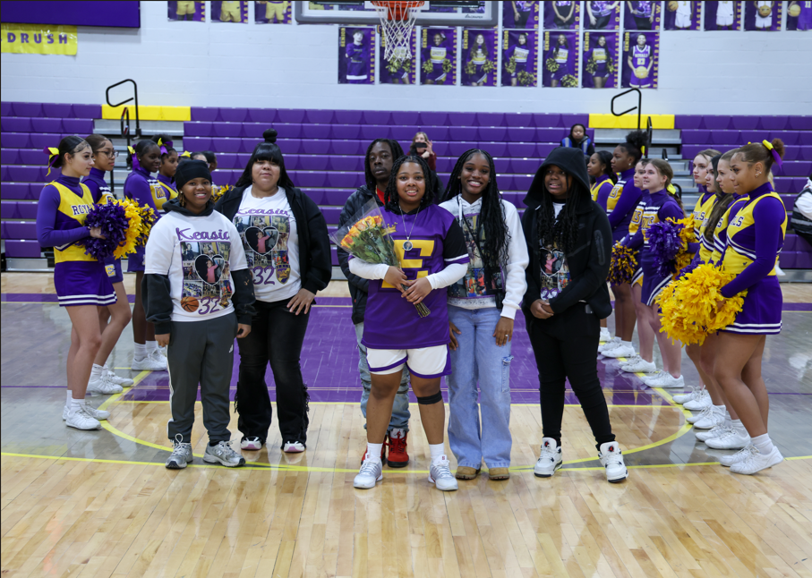 A group of people standing next to a girl in her team uniform and holding flowers.