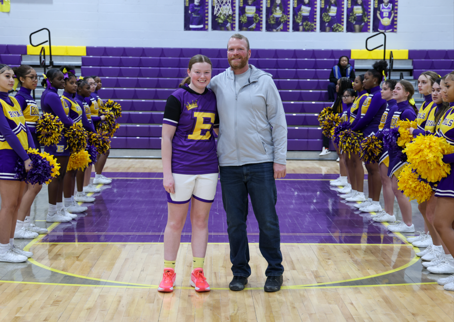 A young girl in her team uniform standing with her dad.