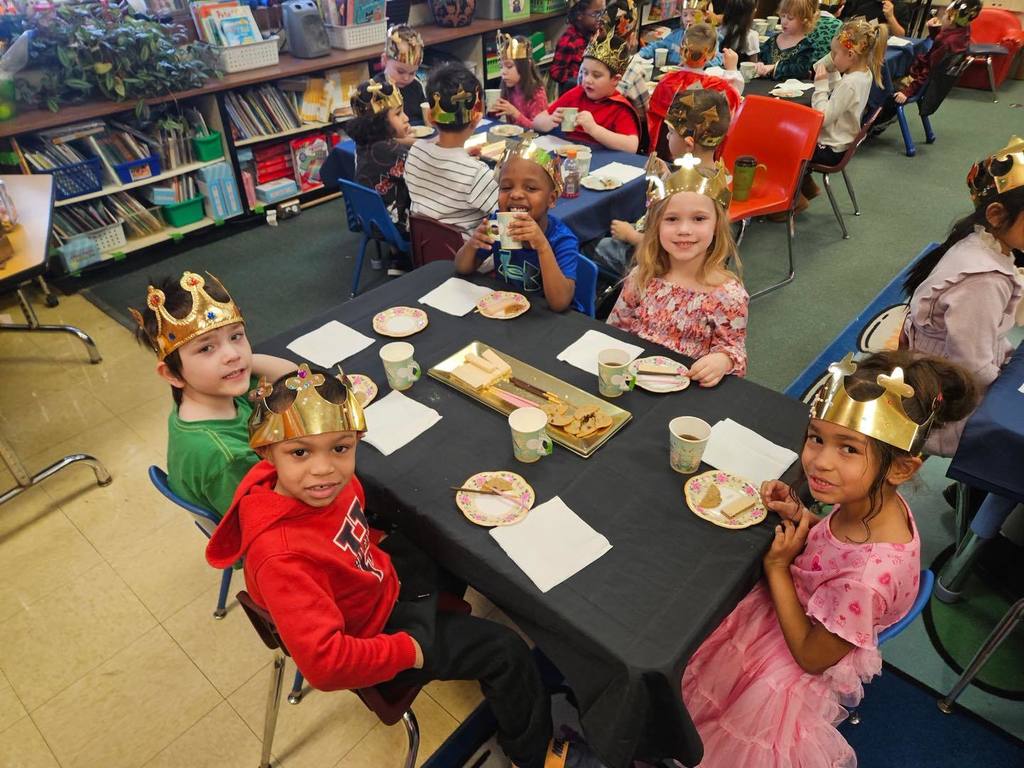 A group of kids wearing gold crowns are sitting at a table with food and drinks on the table. 