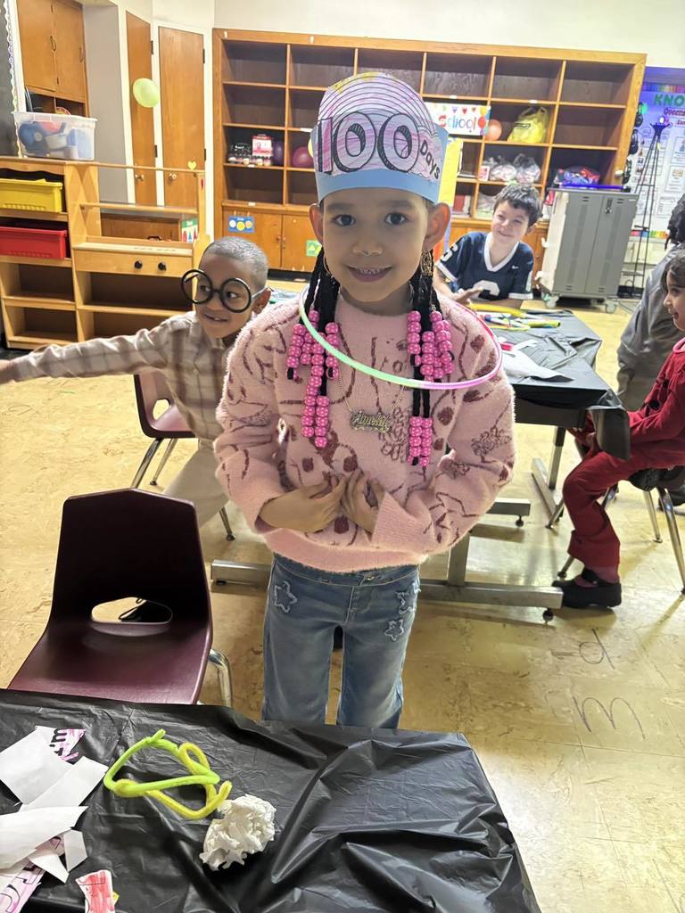 Young girl wearing a paper hat that says 100 days brighter on it. 