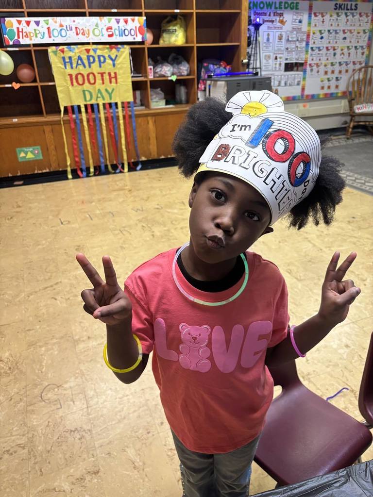 Young girl wearing a paper hat that says 100 days brighter on it. 