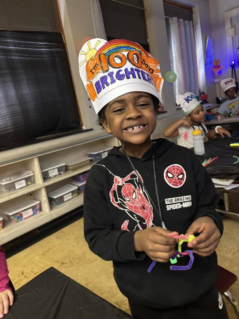 Young boy wearing a paper hat that says 100 days brighter on it. 