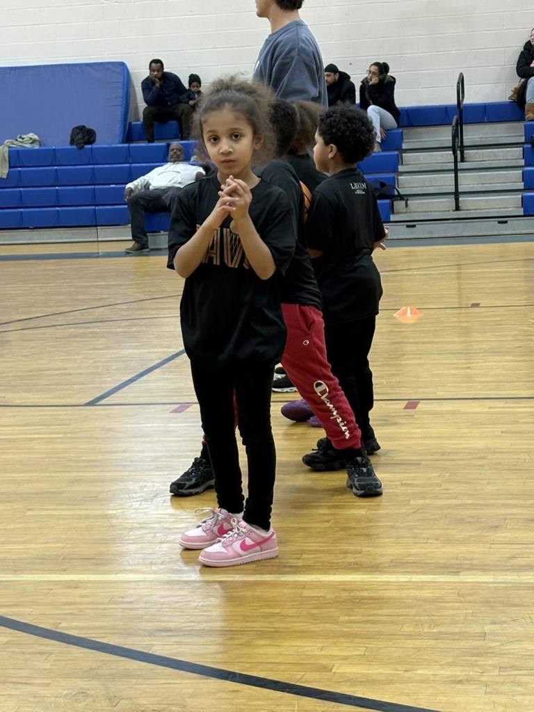 Young girl in a black shirt standing on a basketball court. 