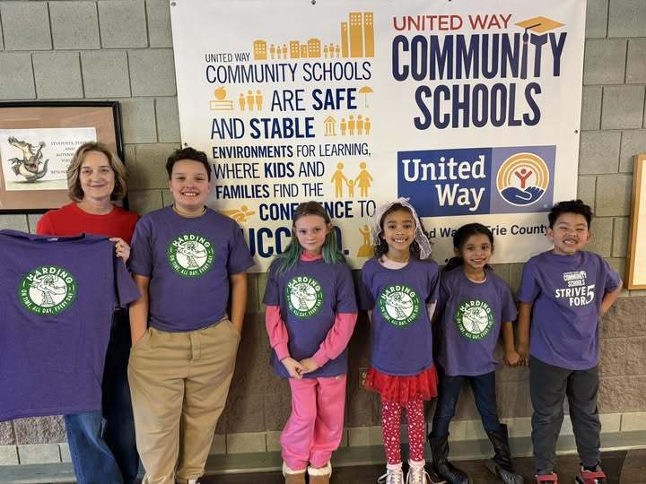 Kids wearing matching purple shirts and women standing on the left holding the same purple shirt.