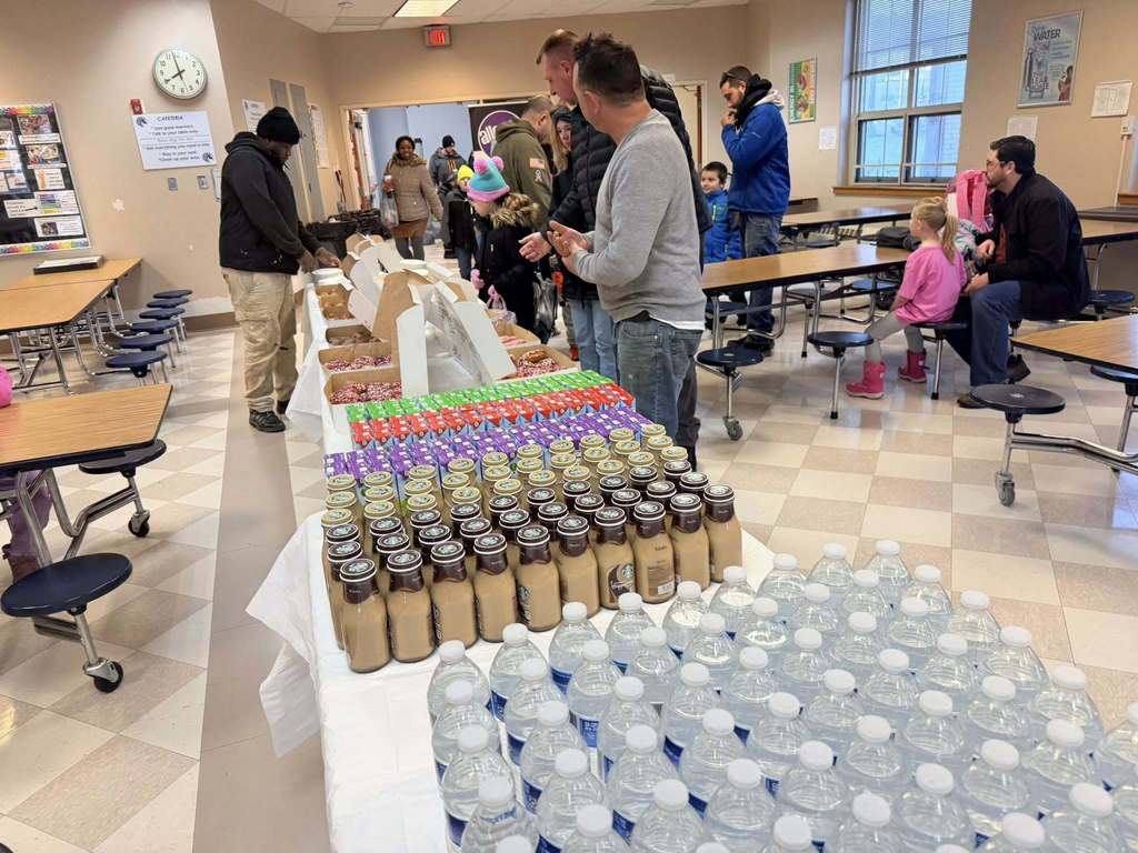Donuts and beverages on a long table in a cafeteria. 