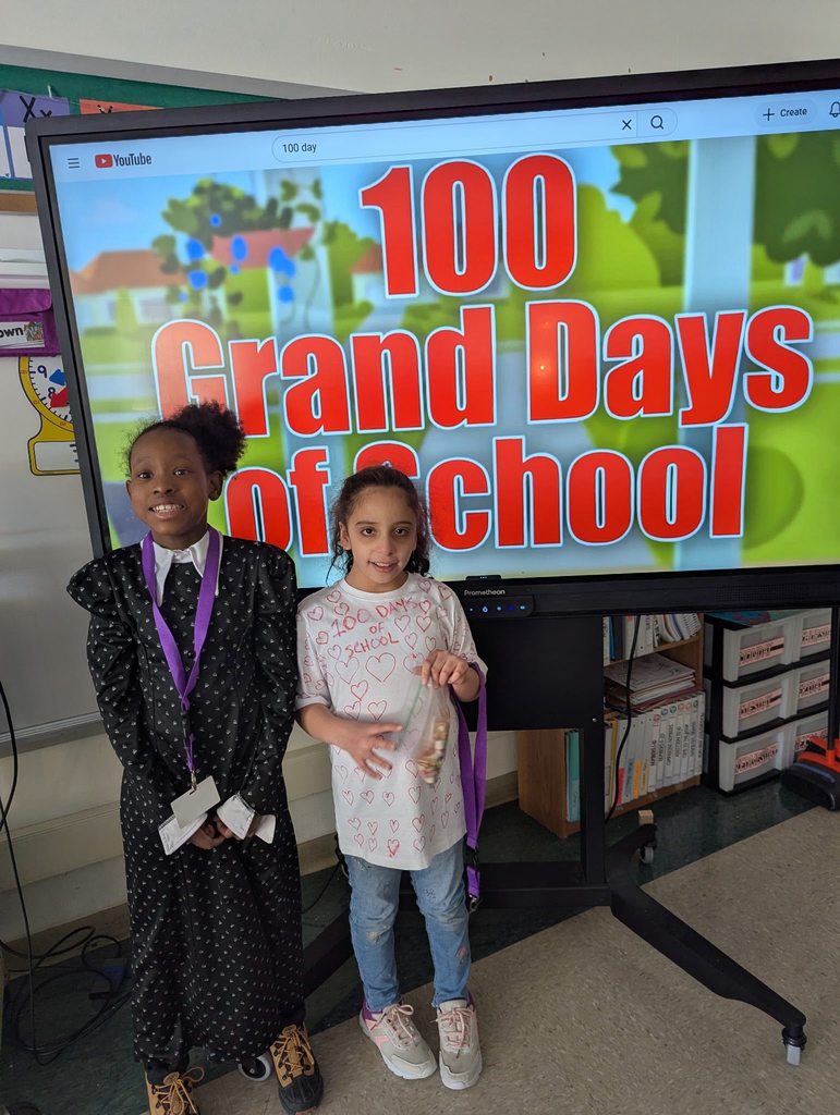 Two young students standing in front of a screen that says 100 grand days of school. 
