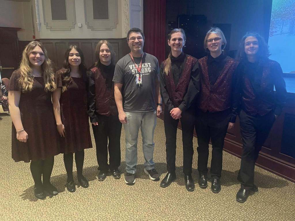 Students in matching maroon vests and dresses standing next to a man in a gray shirt. 